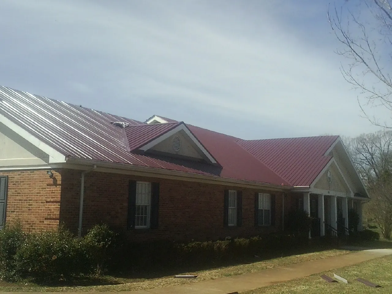Red metal roof with gabled entries on a long brick building, from a Hail Damage Roof Repair job in Newton Falls