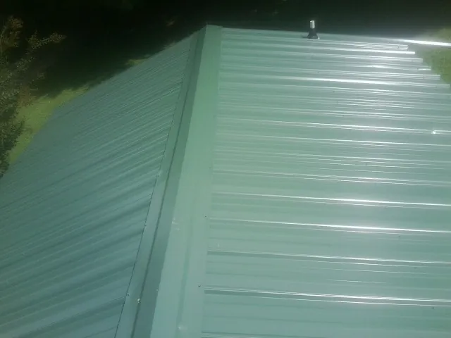 New green metal panels meeting at the ridge of a roof — Flat Roof Repair work by our crew in Newton Falls