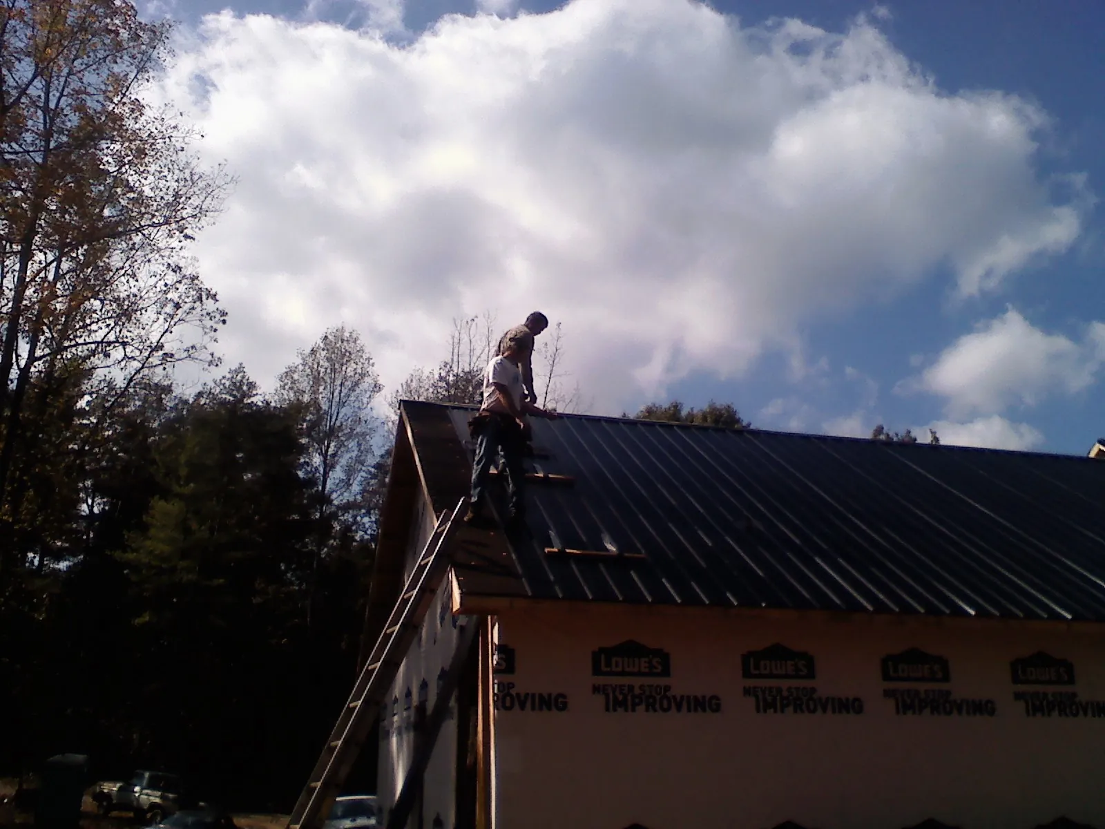 Roofer fastening dark metal panels high against a cloudy sky in Newton Falls