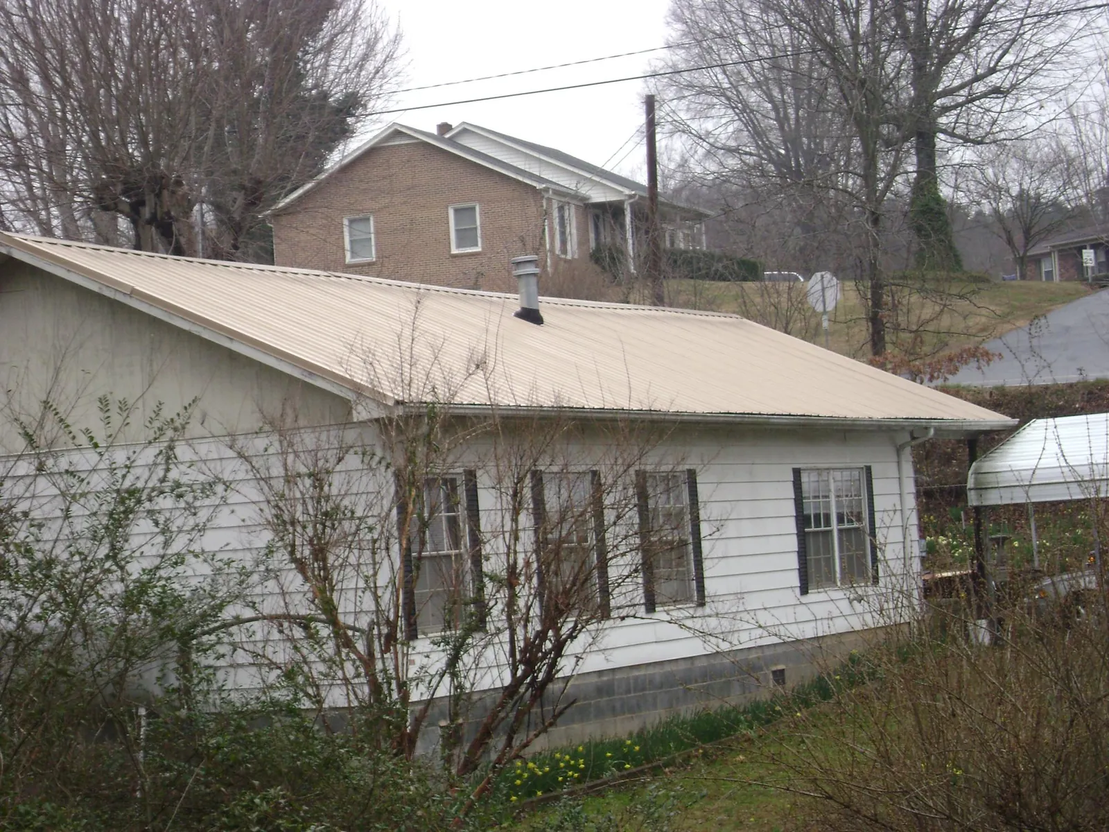 Tan metal roof on a white sided house set into a hillside — Commercial Roofing by Roofing Brothers in Newton Falls