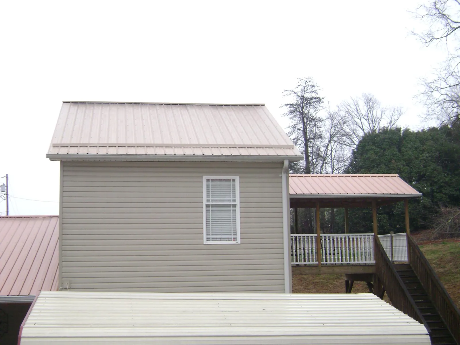 Tan metal roofs on a two story addition and attached porch, from a Roof Replacement job in Newton Falls